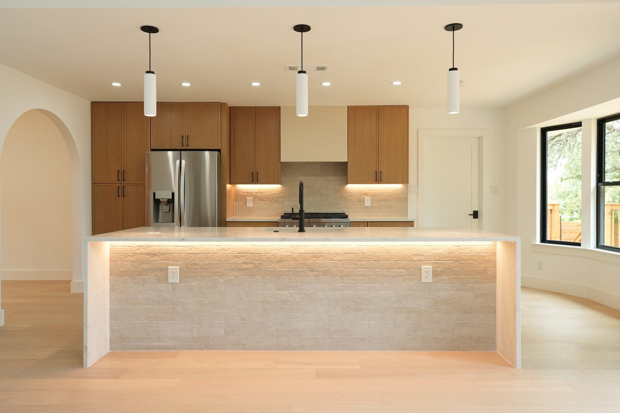 The same kitchen finished, wood cabinets and a lit waterfall island